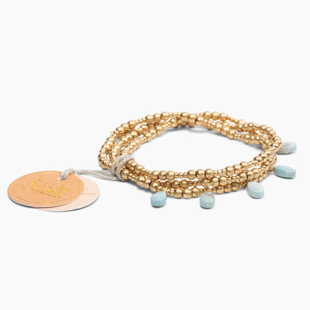 Gold beaded bracelet with blue beads and a tag on a white background