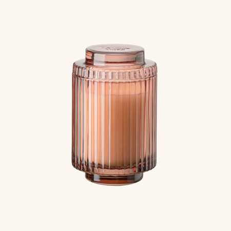 Rose gold glass candle holder with a candle inside on a white background