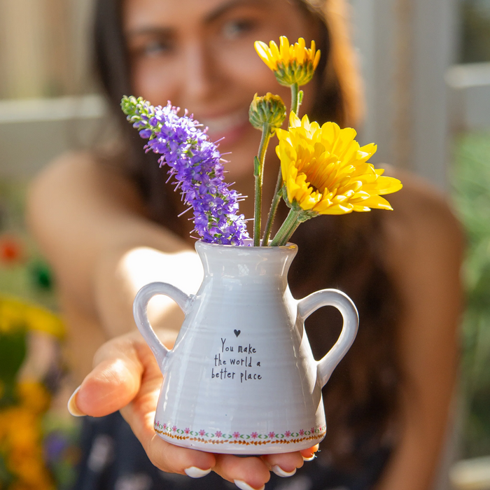 Person holding a small white vase with flowers, blurred background