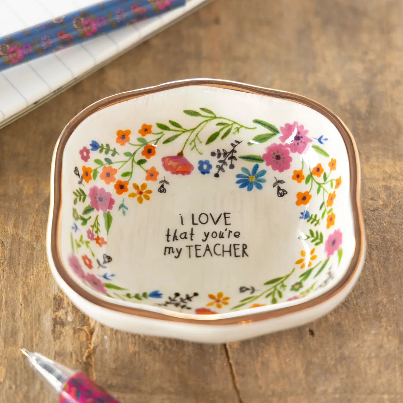 Decorative dish with floral design and 'I love that you're my teacher' text on a wooden surface.