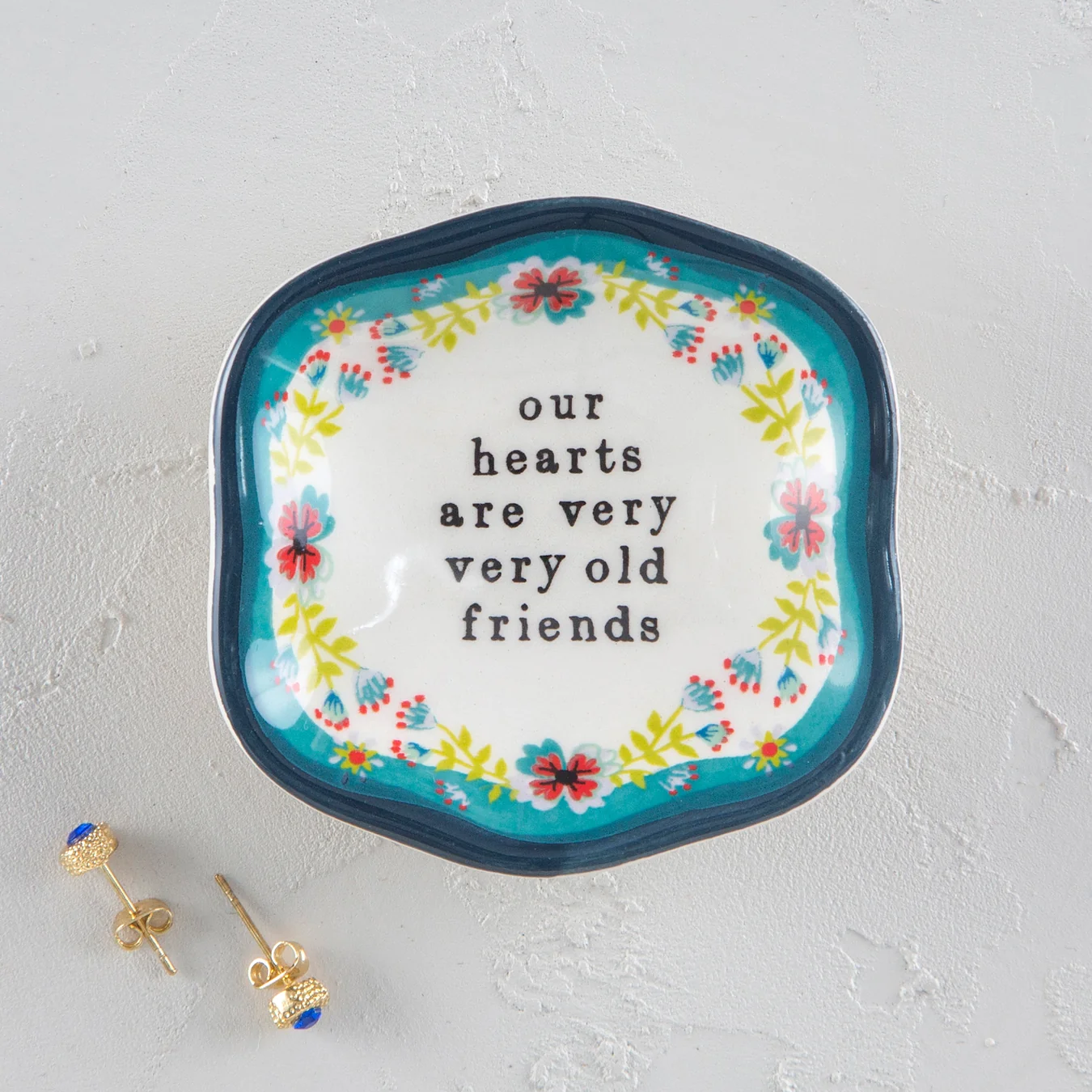 Mini trinket dish with the words "our hearts are very very old friends". White dish with a floral design and blue rim.