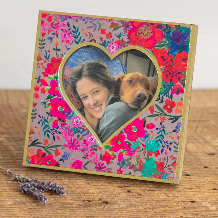 Colorful floral photo frame with a heart-shaped cutout featuring a person and a dog on a wooden surface.
