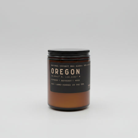 Candle jar labeled 'Oregon' with a black lid on a white background