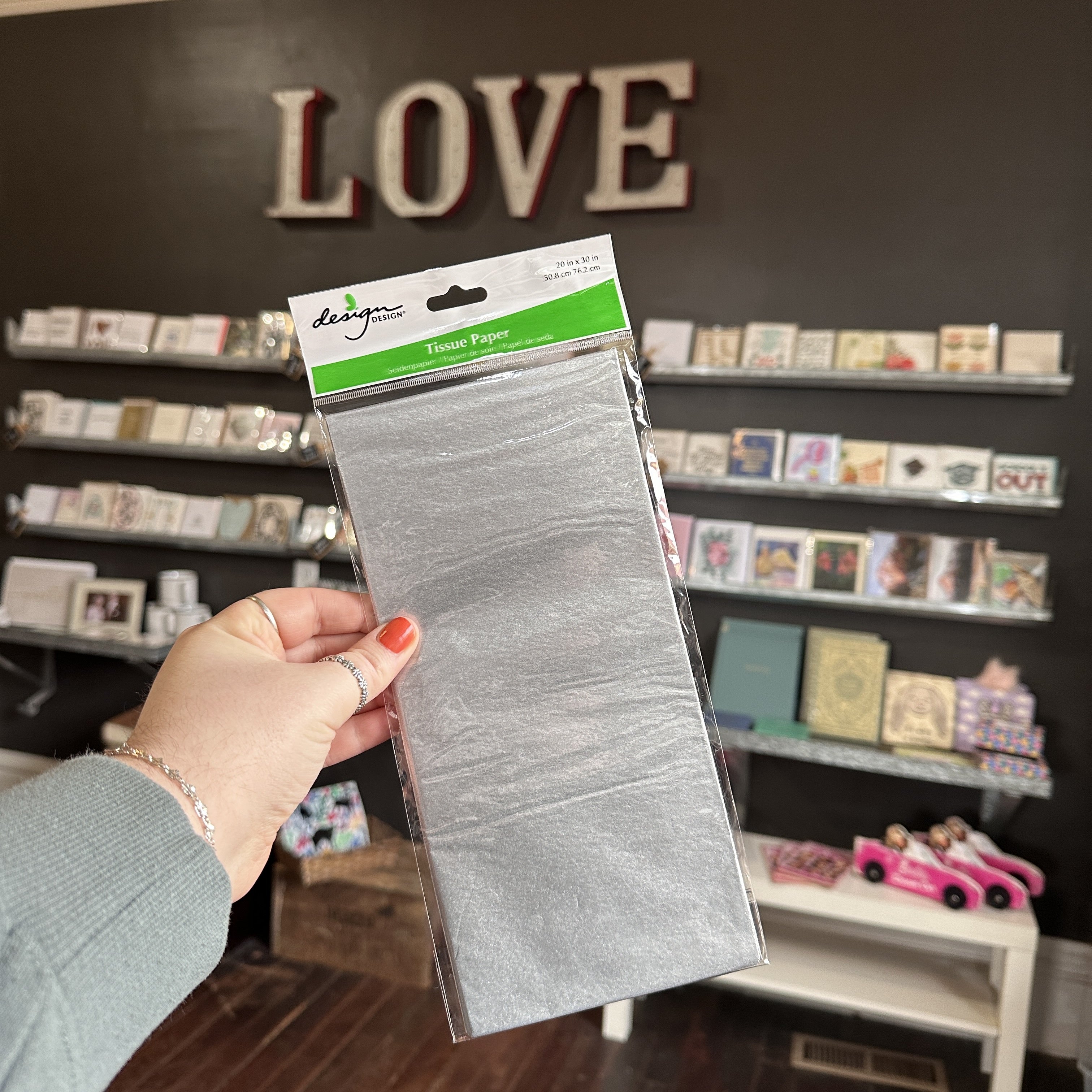 Hand holding a package of silver tissue paper with a store interior in the background