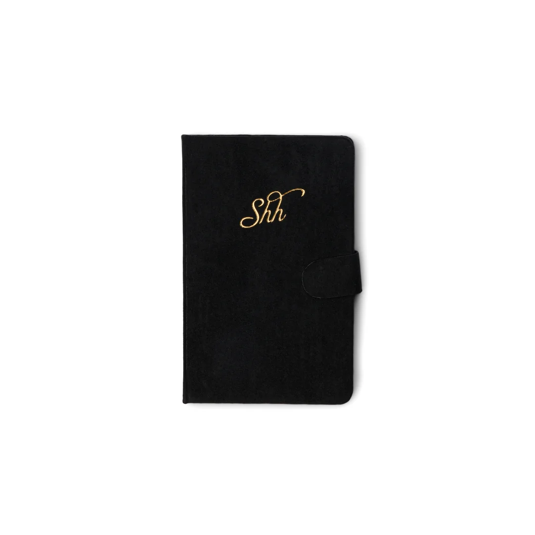 A black textured folio-style notebook or wallet with a gold cursive 'Shh' monogram on the front and a side tab closure, shown on a plain white background.