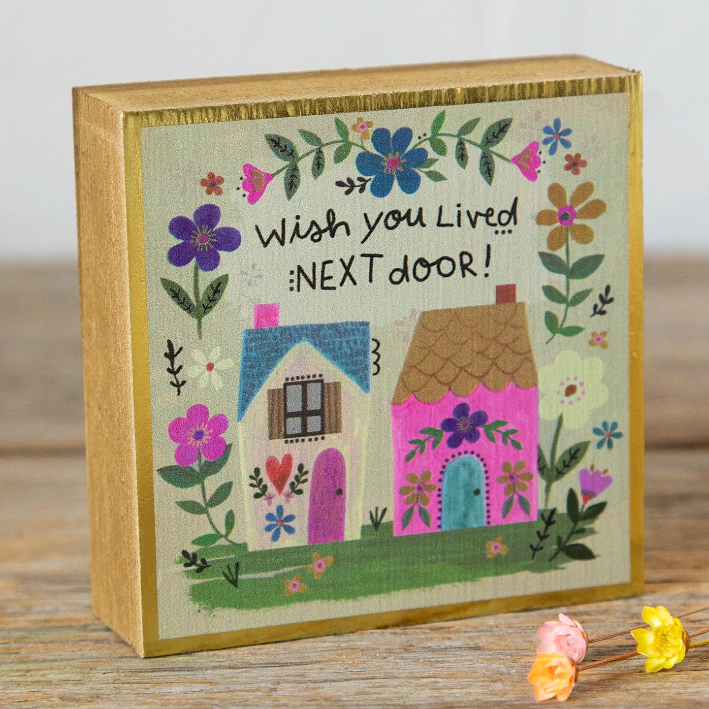 Decorative box with houses and flowers on a wooden surface that says "wish you lived next door"