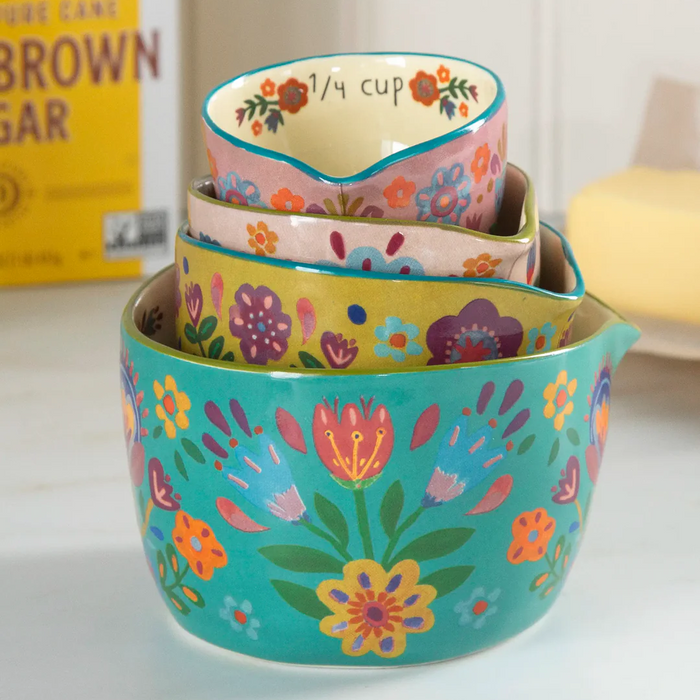 Set of colorful floral-patterned measuring cups on a white surface with a box of brown sugar in the background.