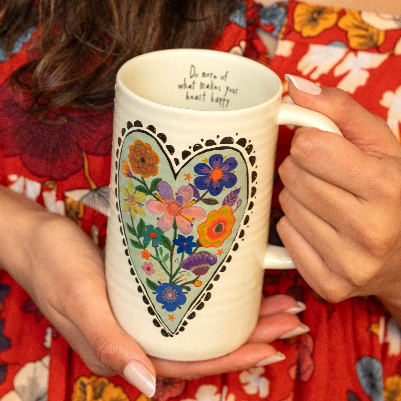 Person holding a mug with floral design and text, wearing a red floral dress.