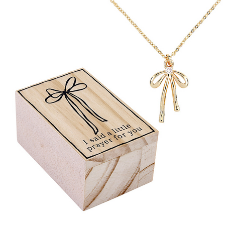 Gold necklace with bow pendant on a wooden box with text