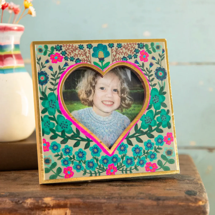 Decorative photo frame with a heart-shaped cutout featuring a young girl's photo, placed on a wooden surface.