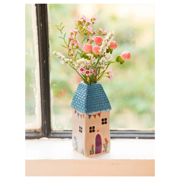 Decorative vase shaped like a house with flowers on a windowsill