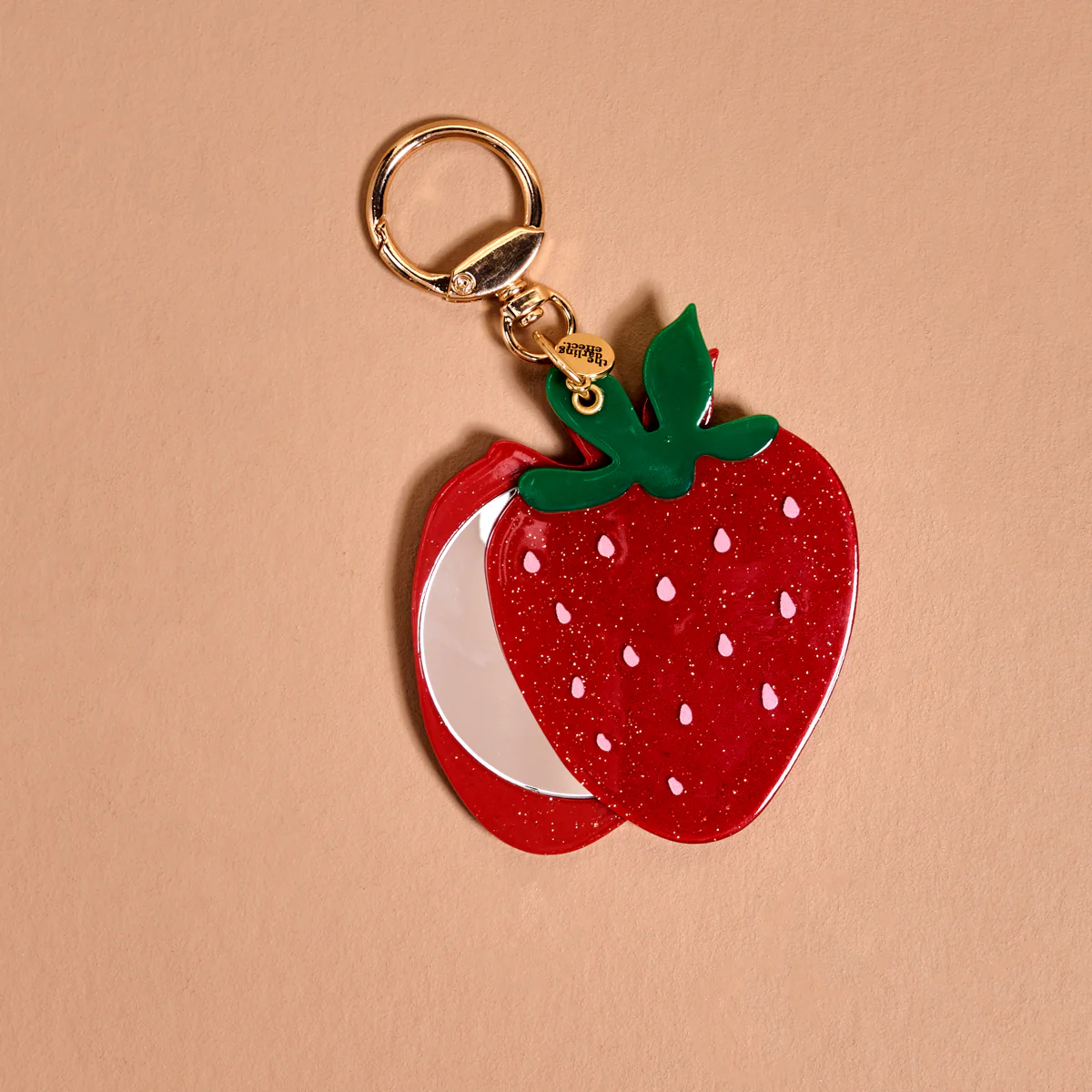 Strawberry-shaped keychain mirror on a beige background