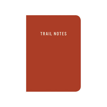 A rust-red hardcover notebook with rounded corners and the words 'TRAIL NOTES' printed in white at the top center, shown on a plain white background.