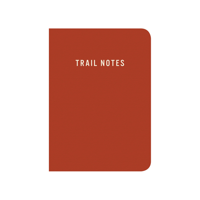 A rust-red hardcover notebook with rounded corners and the words 'TRAIL NOTES' printed in white at the top center, shown on a plain white background.