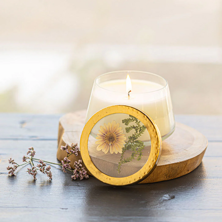 Candle in a glass holder with a decorative coaster featuring a pressed flower on a wooden surface.