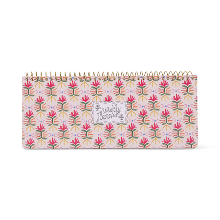 A weekly planner notebook with a colorful floral pattern on a light pink cover, bound with a gold spiral, shown against a plain white background.