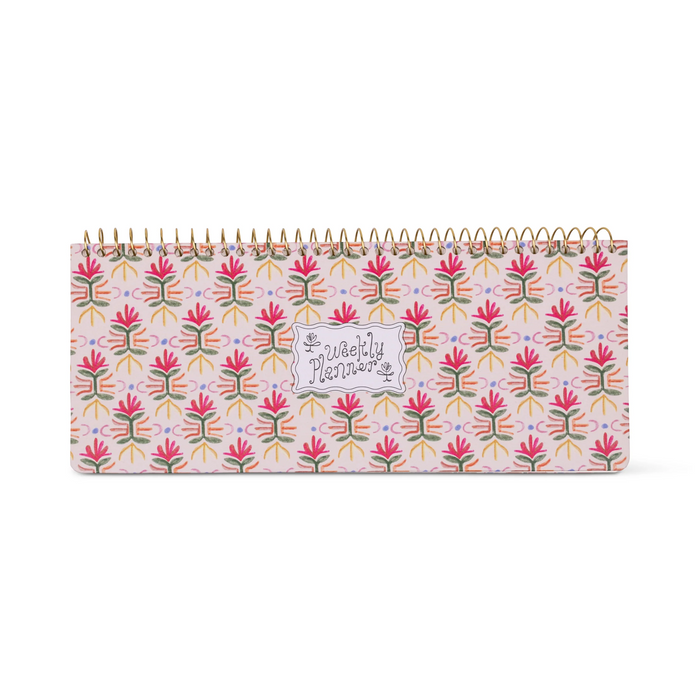 A weekly planner notebook with a colorful floral pattern on a light pink cover, bound with a gold spiral, shown against a plain white background.