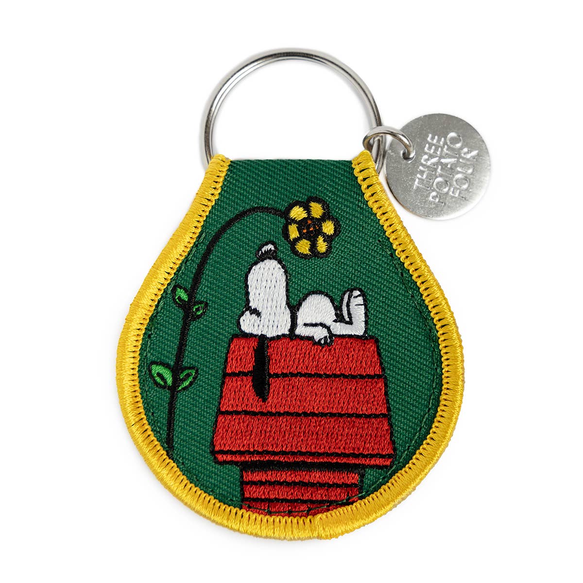 Keychain with Snoopy and a flower on a doghouse design, featuring a green background and yellow border.