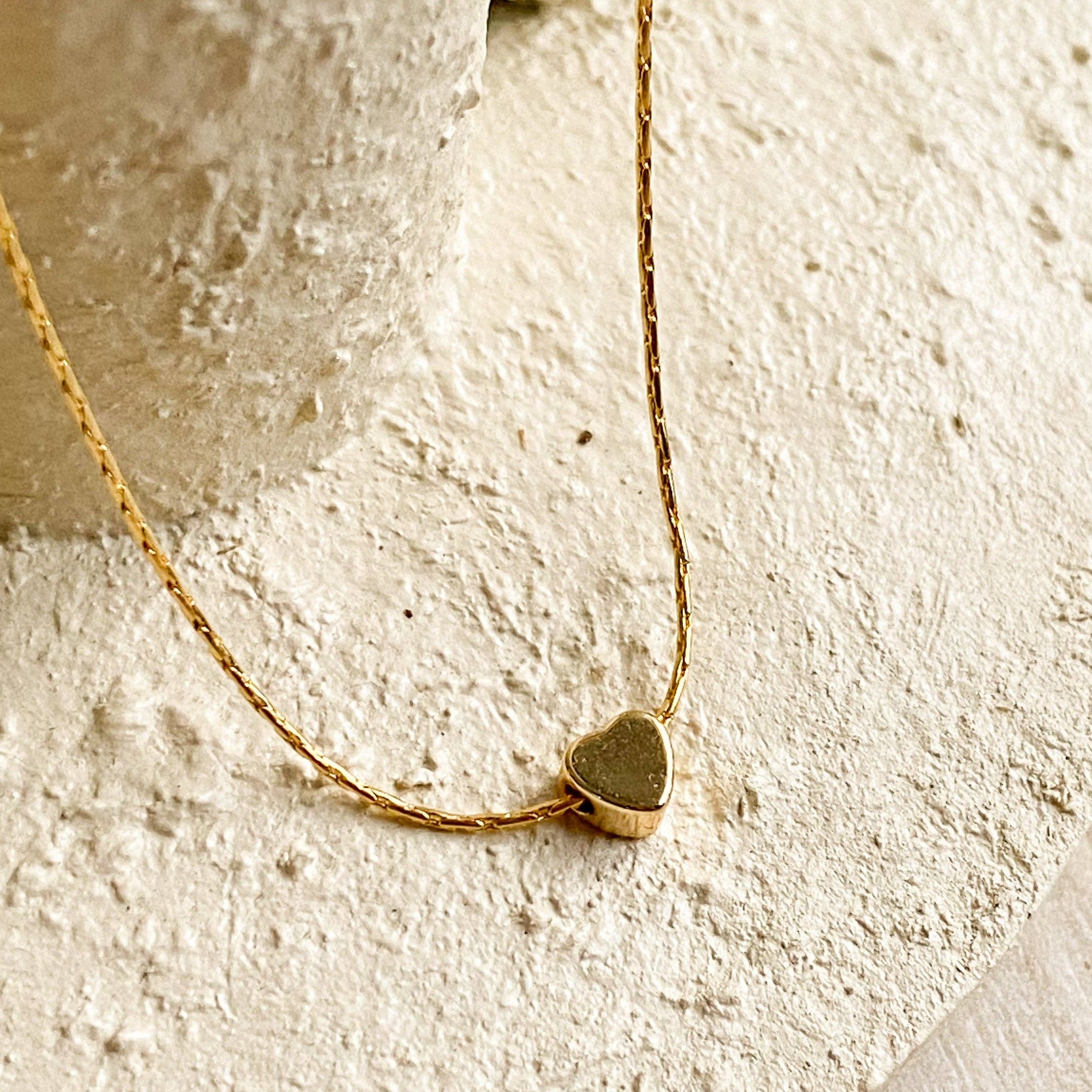 Gold heart-shaped necklace on a textured beige surface