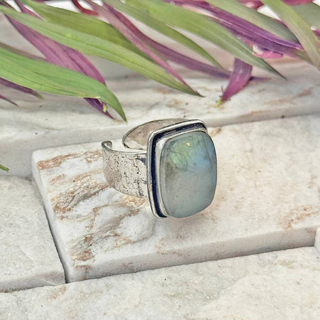 Silver ring with a green stone on a marble surface with plants in the background