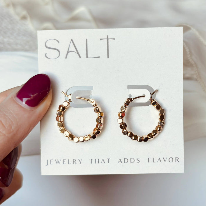 Gold hoop earrings on a 'SALT' branded card held by a hand with maroon nail polish.