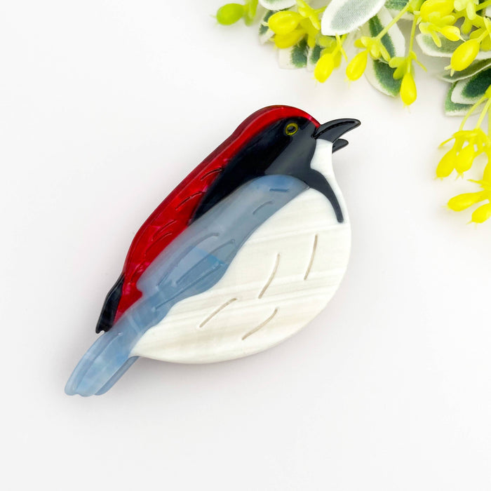 Decorative bird hair clip with red, black, and blue colors on a white background with yellow flowers.