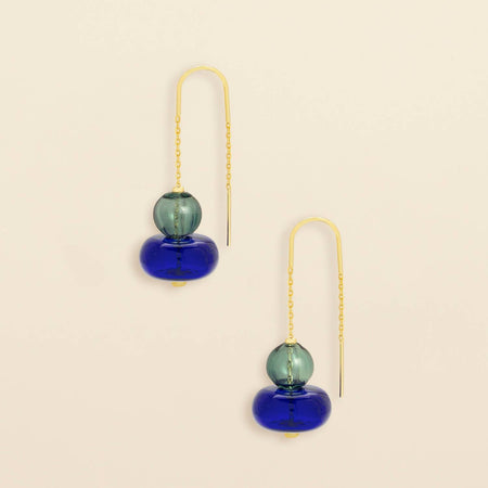 Pair of earrings with blue and green glass beads on gold chains against a beige background