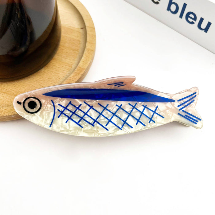 Decorative fish-shaped hair clip with blue and black patterns on a white surface.