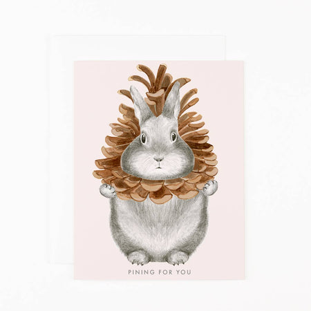 Illustration of a rabbit wearing a pine cone hat on a pink background. Reads " Pining for you"