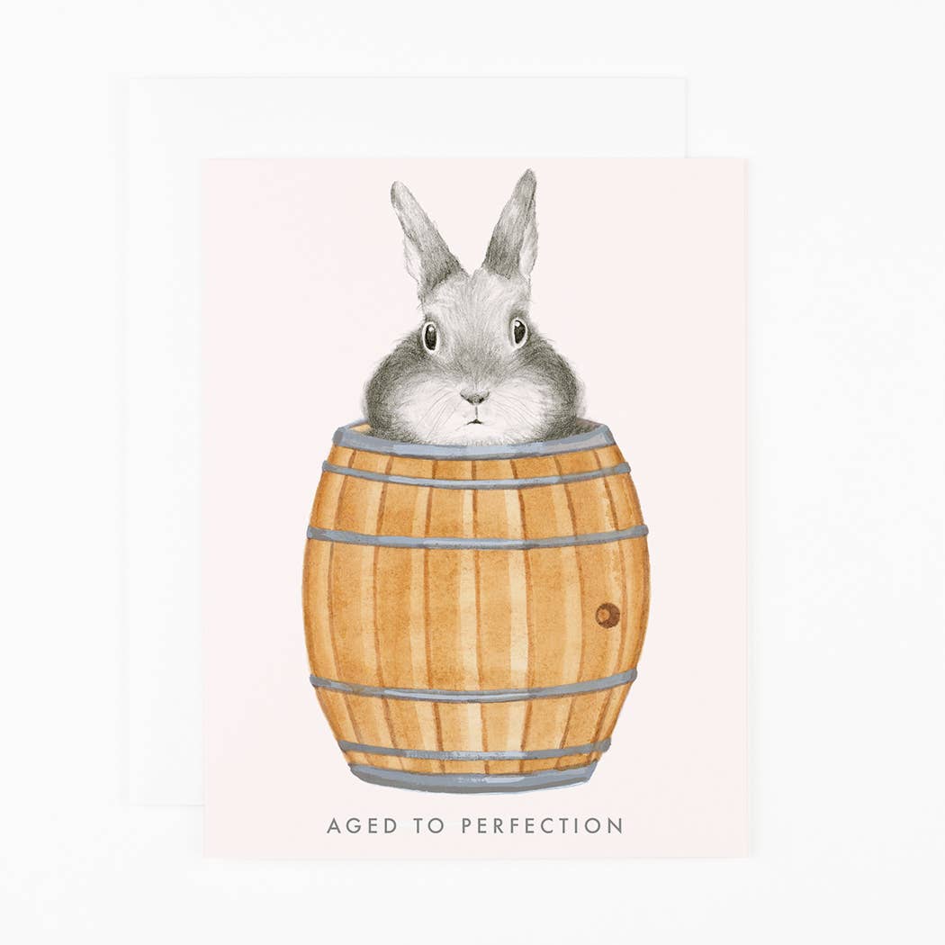 Illustration of a rabbit inside a wooden barrel with 'Aged to Perfection' text on a light pink background