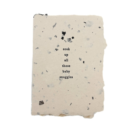 A rectangular handmade paper card or with a speckled terracotta texture and the text 'soak up all those baby snuggles' printed in the center, shown on a plain white background.