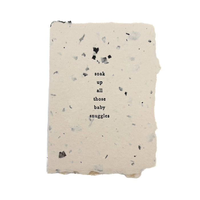 A rectangular handmade paper card or with a speckled terracotta texture and the text 'soak up all those baby snuggles' printed in the center, shown on a plain white background.