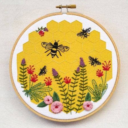 Embroidery hoop with a bee and floral design on a yellow hexagonal pattern.