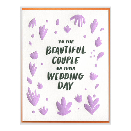 A greeting card with a white textured background, featuring the phrase 'TO THE BEAUTIFUL COUPLE ON THEIR WEDDING DAY' in dark green lettering, surrounded by lavender foil floral and heart-shaped accents and a thin orange border.