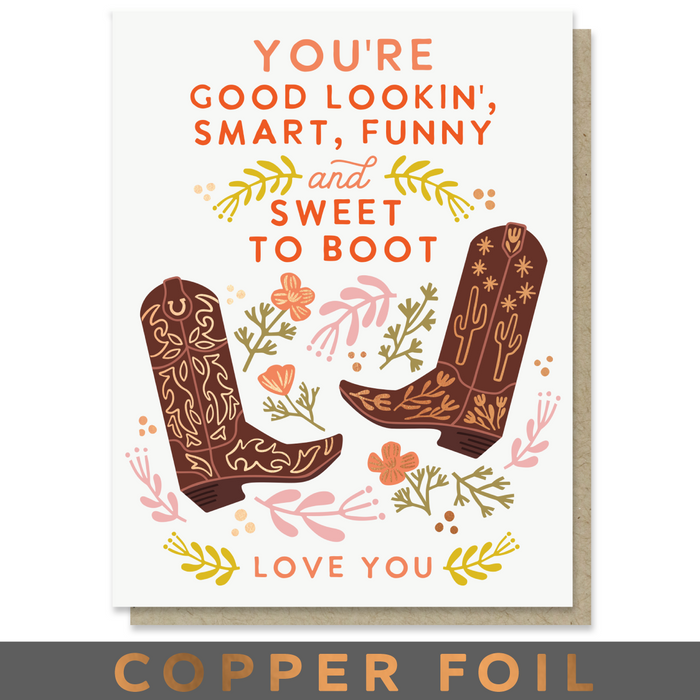 A greeting card with a western theme, featuring the text 'YOU'RE GOOD LOOKIN', 'SMART, FUNNY and SWEET TO BOOT' and 'LOVE YOU' in orange lettering, decorated with illustrated brown cowboy boots, flowers, and leaves. A kraft envelope is visible behind the card, and a dark banner at the bottom reads 'COPPER FOIL'.