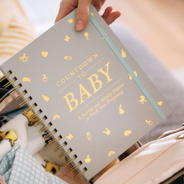 Gray notebook with 'Countdown to Baby' title and pregnancy symbols, held by a person.