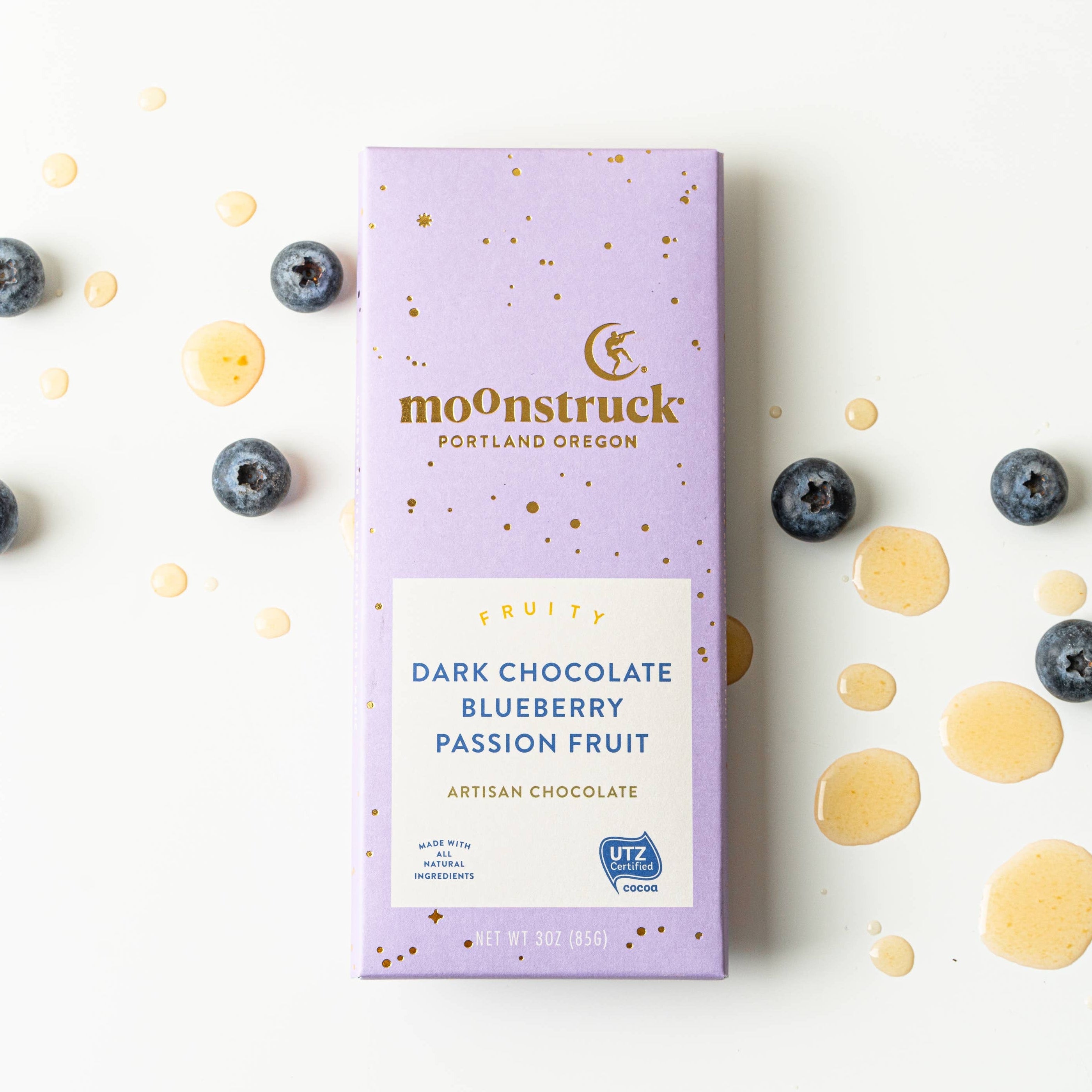 Moonstruck dark chocolate blueberry passion fruit bar packaging on a white background with blueberries and gold drops.