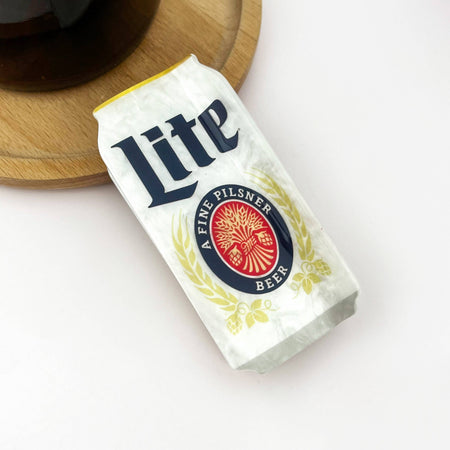 Miller Lite beer can claw clip on a white surface with a wooden coaster in the background