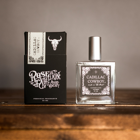 Cadillac Cowboy perfume bottle and packaging on a wooden surface with a neutral background