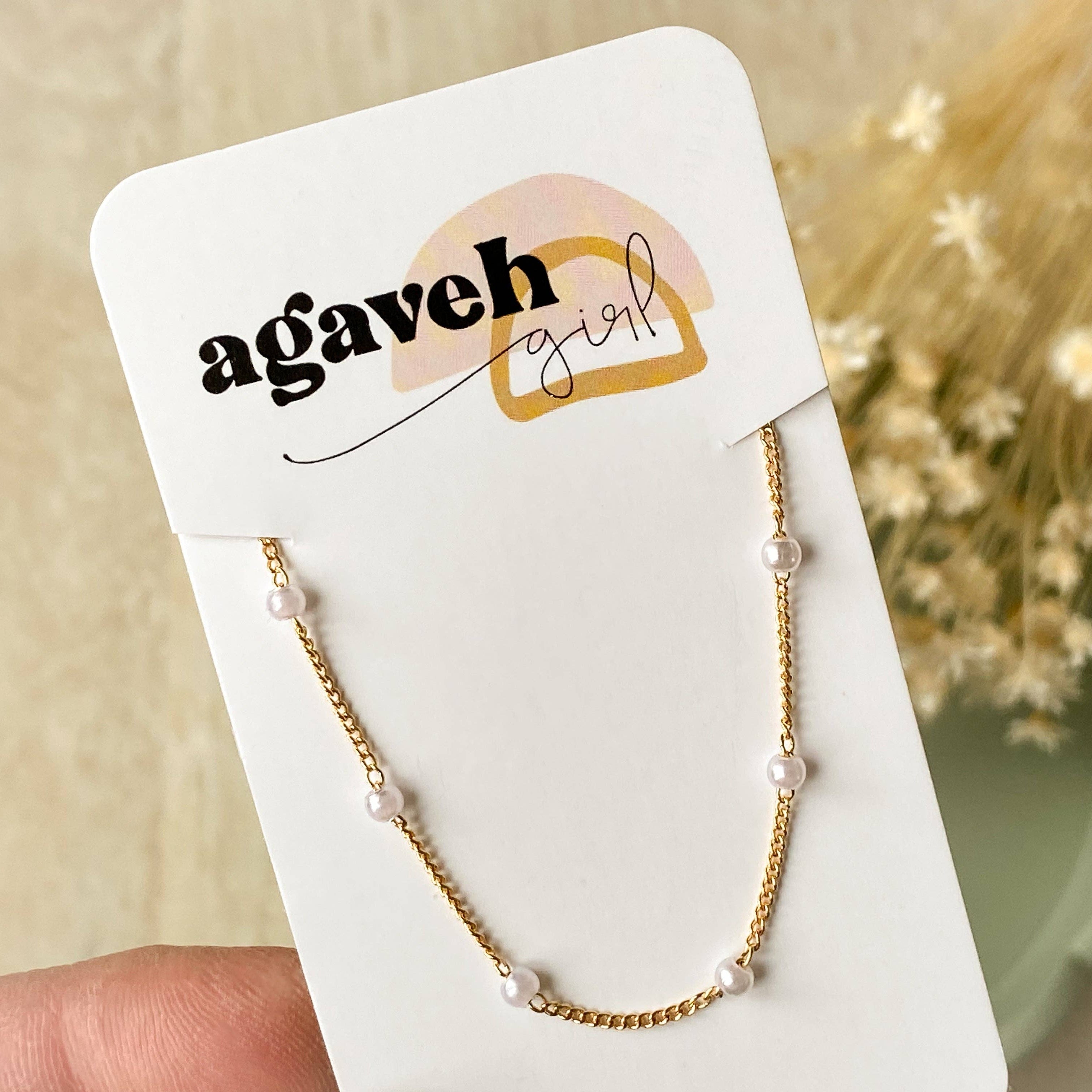 Gold necklace with small pearls on a 'agaveh girl' branded card with flowers in the background