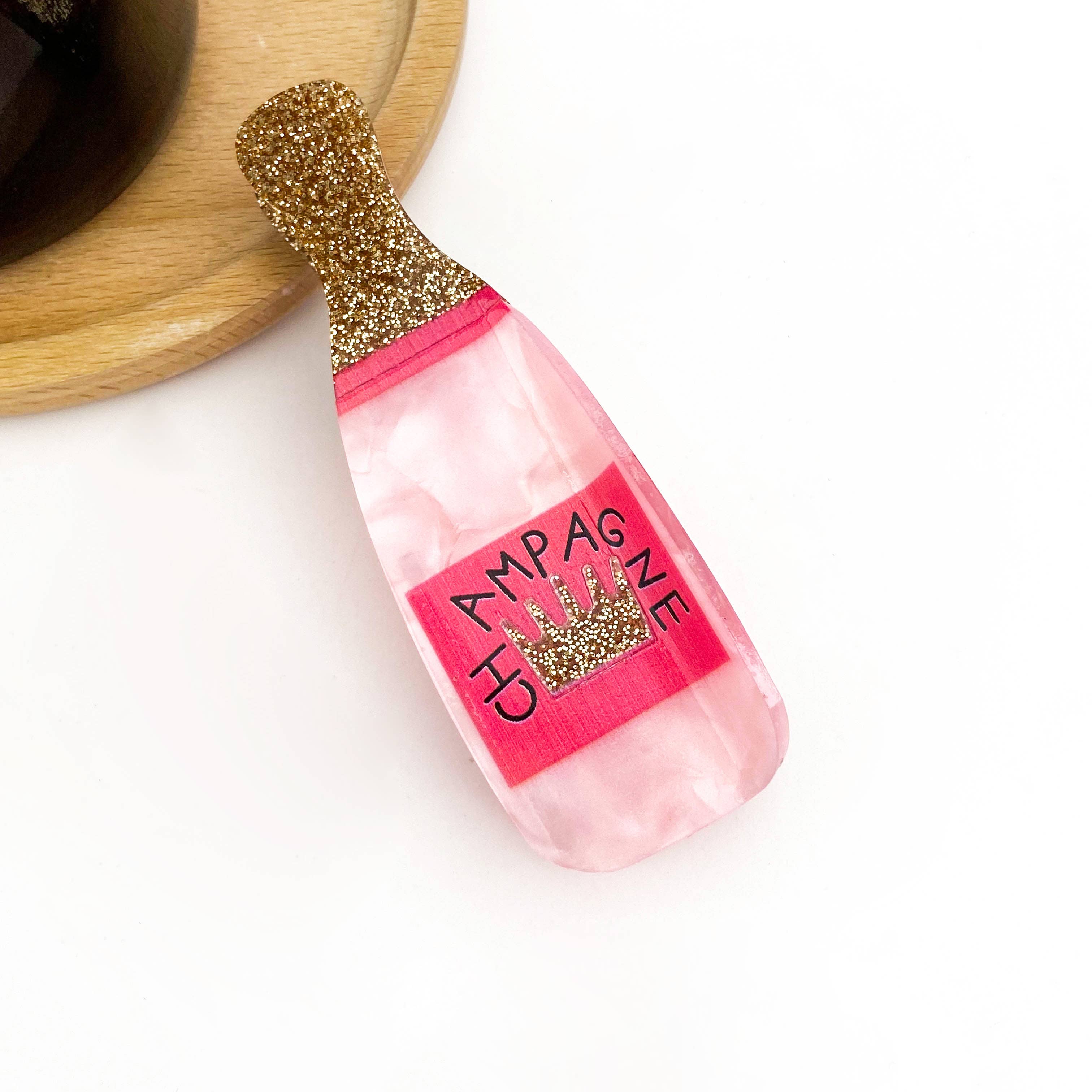Pink bottle-shaped champagne hair clip with gold glitter top on a white background