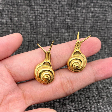 Gold snail-shaped earrings held in a hand against a textured gray background