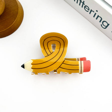 Hair clip shaped like a pencil with a yellow ribbon on a white background