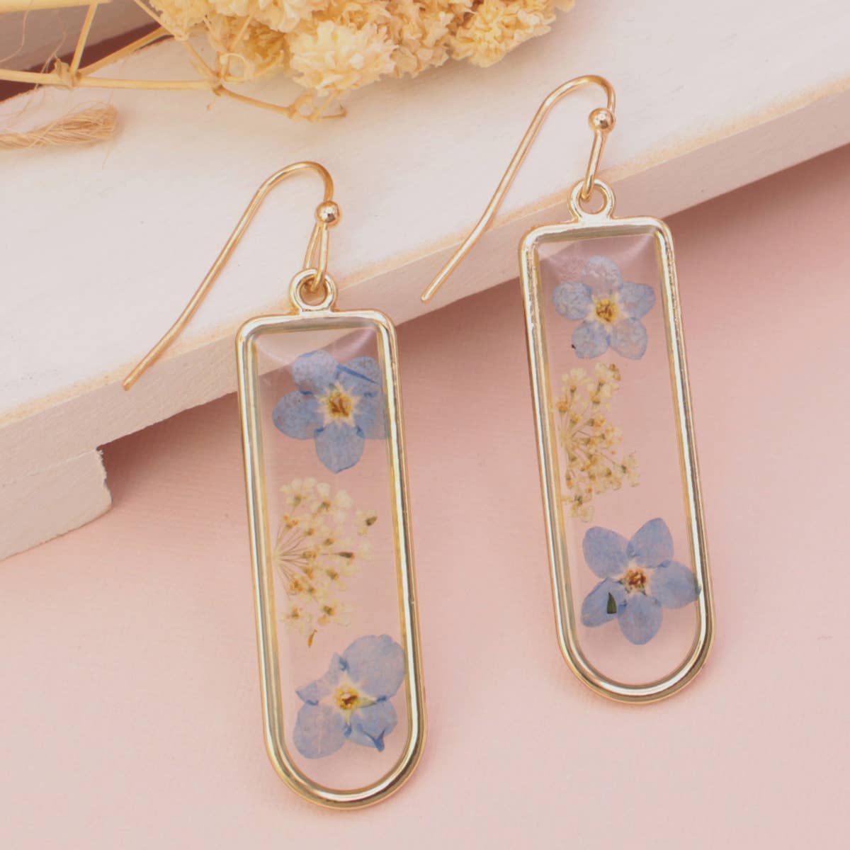 Gold earrings with blue floral elements on a pink background
