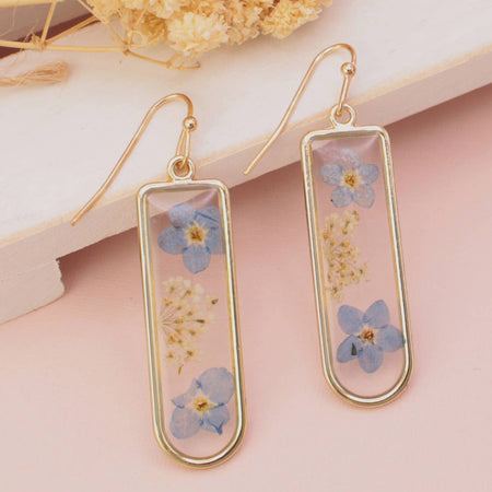 Gold earrings with blue floral elements on a pink background