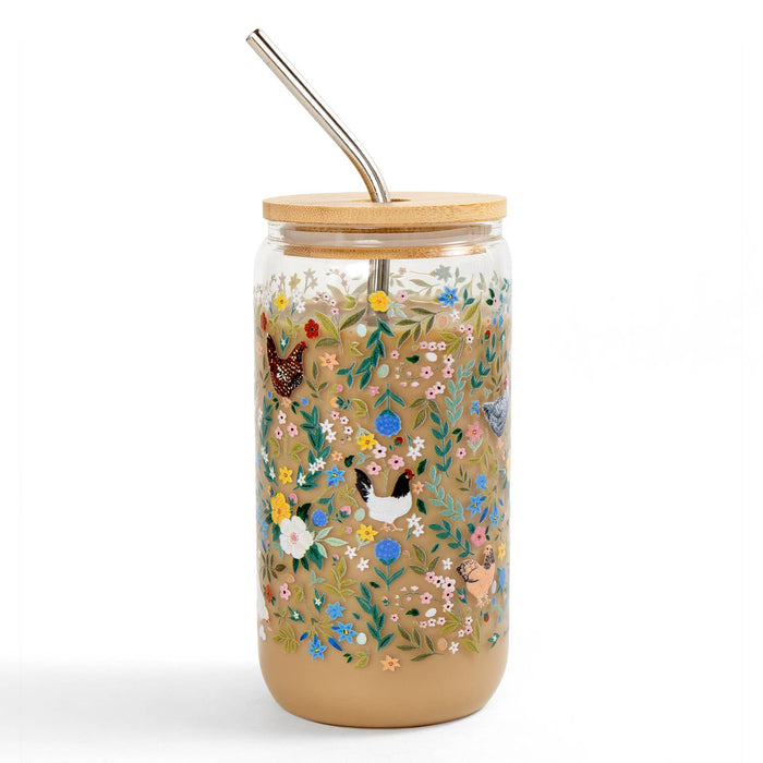 Glass tumbler with floral design, wooden lid, and metal straw on a white background
