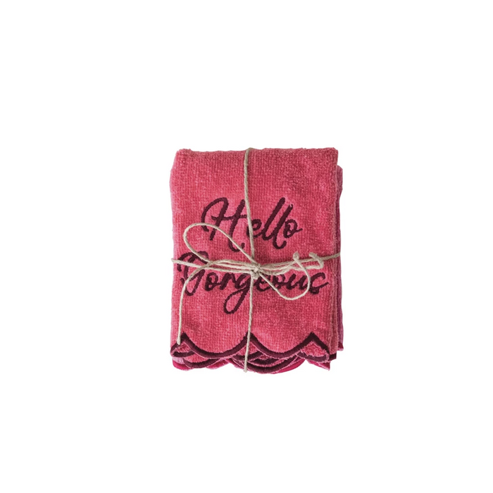 Folded pink towels with 'Hello Gorgeous' text tied with twine on a white background