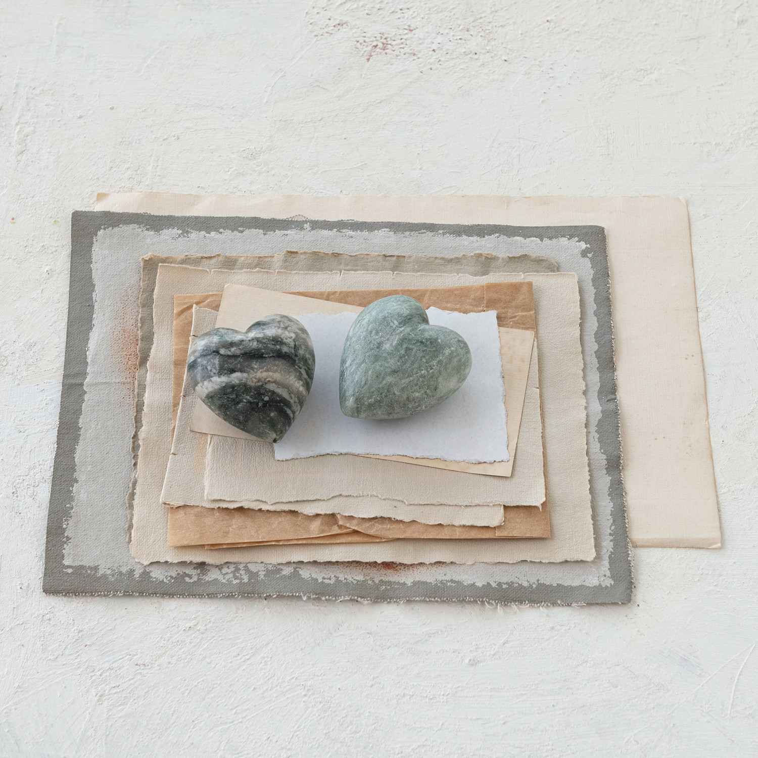Two heart shaped marbles on top of textured paper with a white background