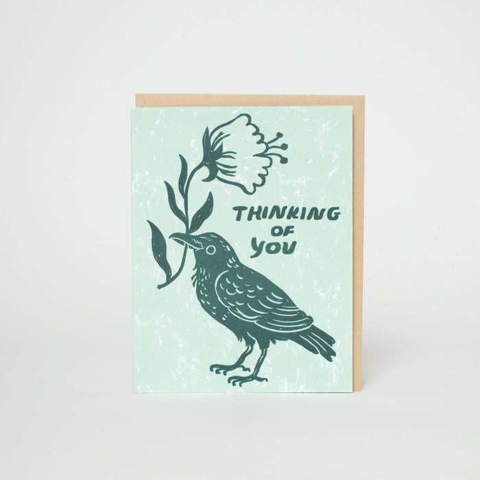 Greeting card with a bird and flower illustration and 'Thinking of you' text on a light blue background.