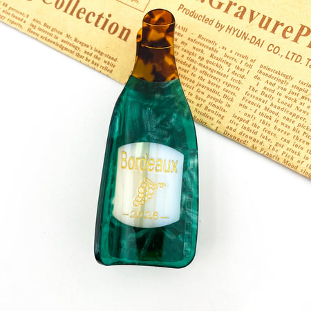 Green bottle-shaped hair clip with 'Bordeaux' label on a white background